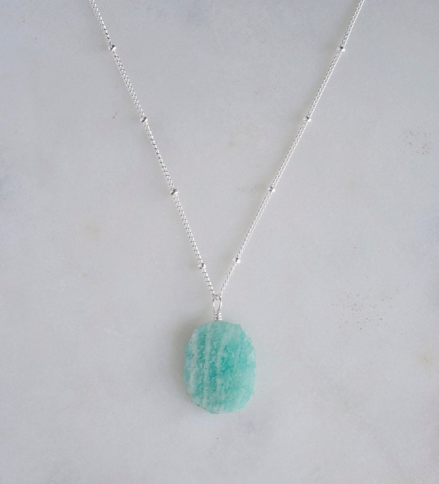 Aqua blue amazonite slice gemstone set onto a sterling silver chain. The stone is semi oval in shape, but irregular. It's smooth polished, but with raw edges.