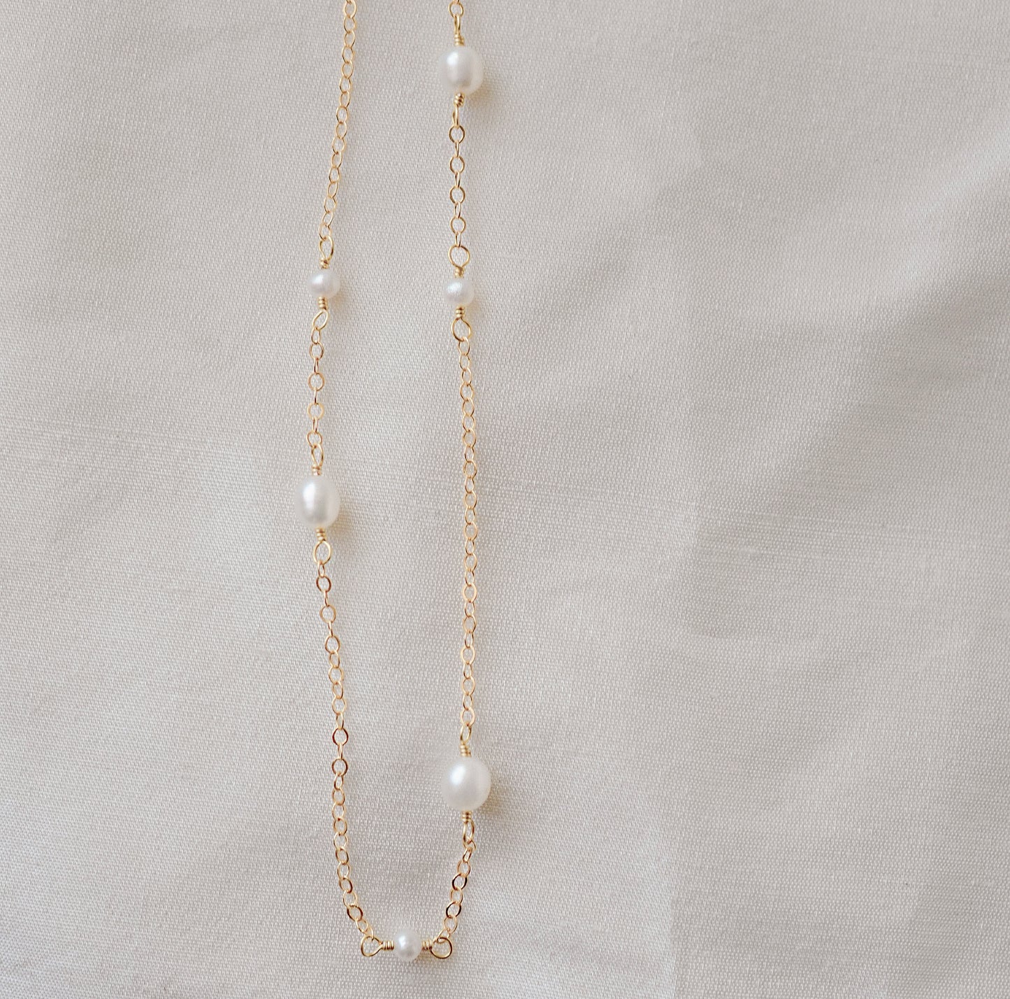 Genuine white freshwater pearls of varying sizes alter on this chain necklace. The gold style is shown.
