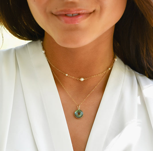Close-up of a woman wearing a handcrafted artisan gold labradorite donut necklace with white freshwater pearl necklace chain.