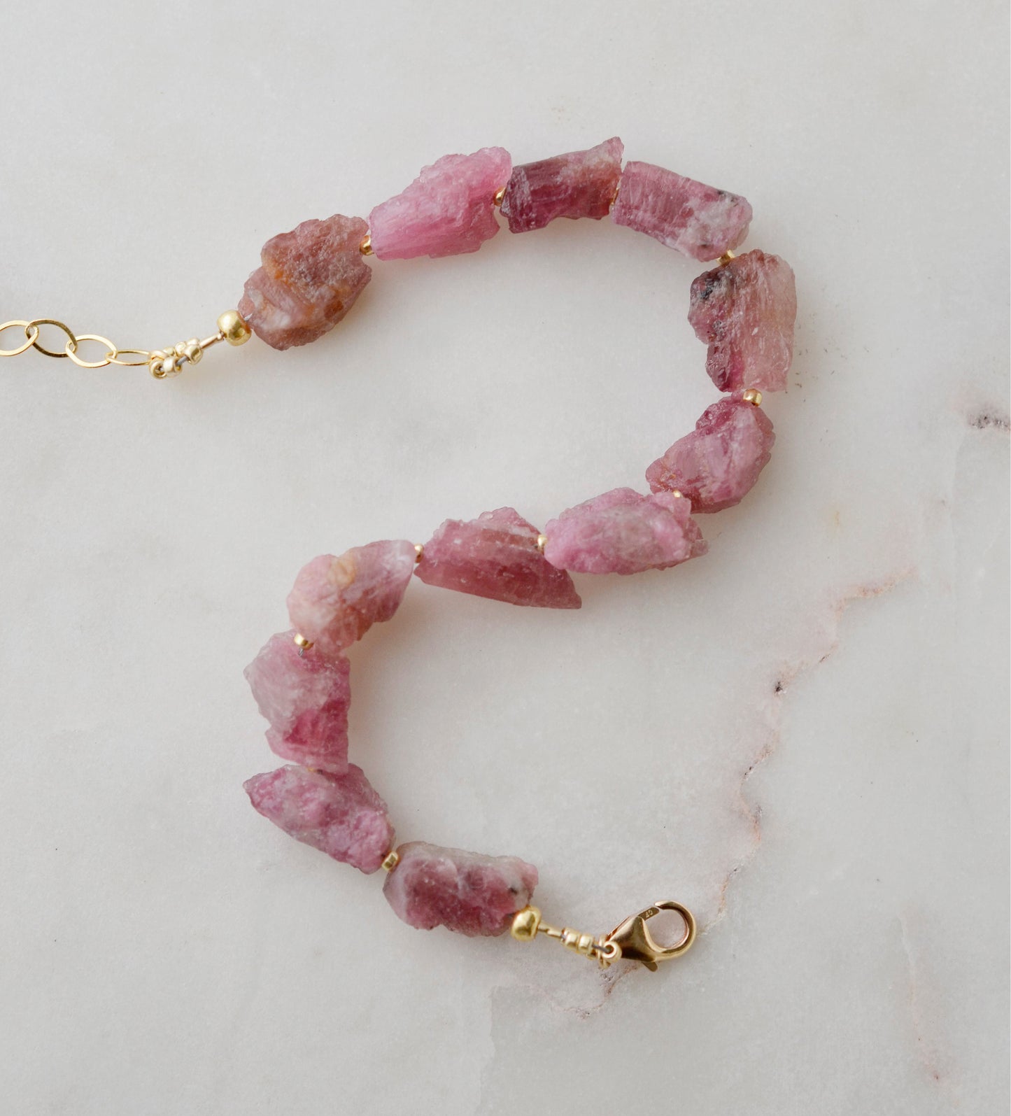 Raw pink tourmaline bracelet with tiny gold beads in-between each stone. The adjustable style is shown.