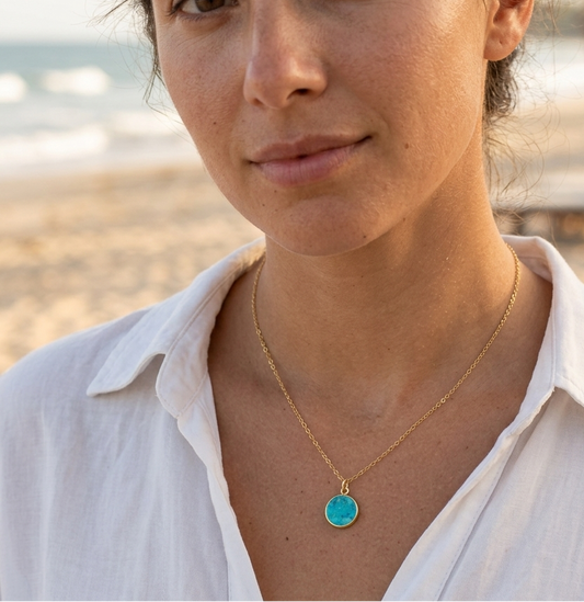 Woman wearing a gold necklace with a turquoise stone pendant. This jewelry is handmade in Connecticut by Gemnia.