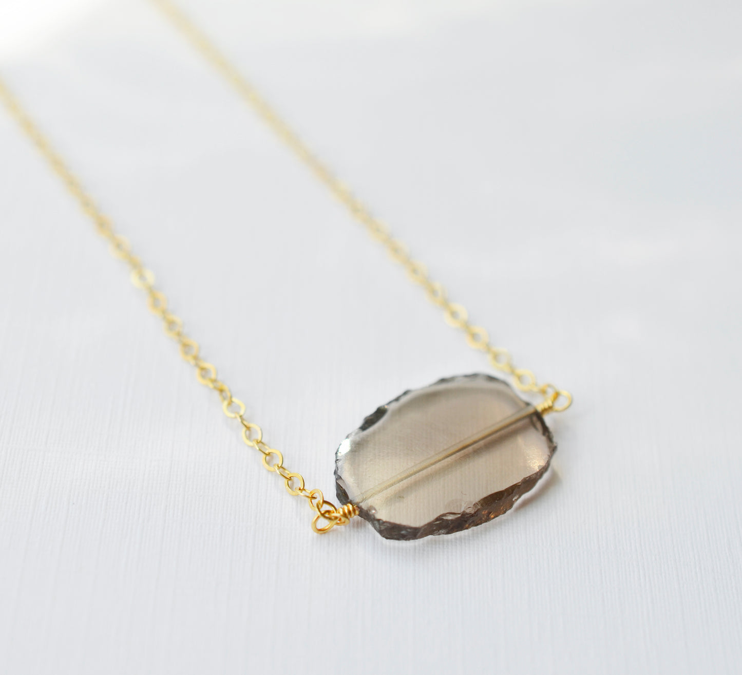 An irregular oval shape, smooth polished Smokey Quartz stone set onto a 14k gold filled chain. The stones edges are raw and irregular.