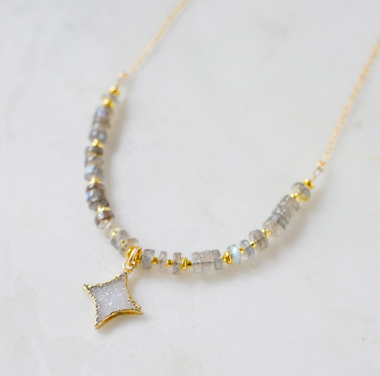 A beaded labradorite gemstone necklace with a white quartz druzy north star pendant at its center. Shown in gold.