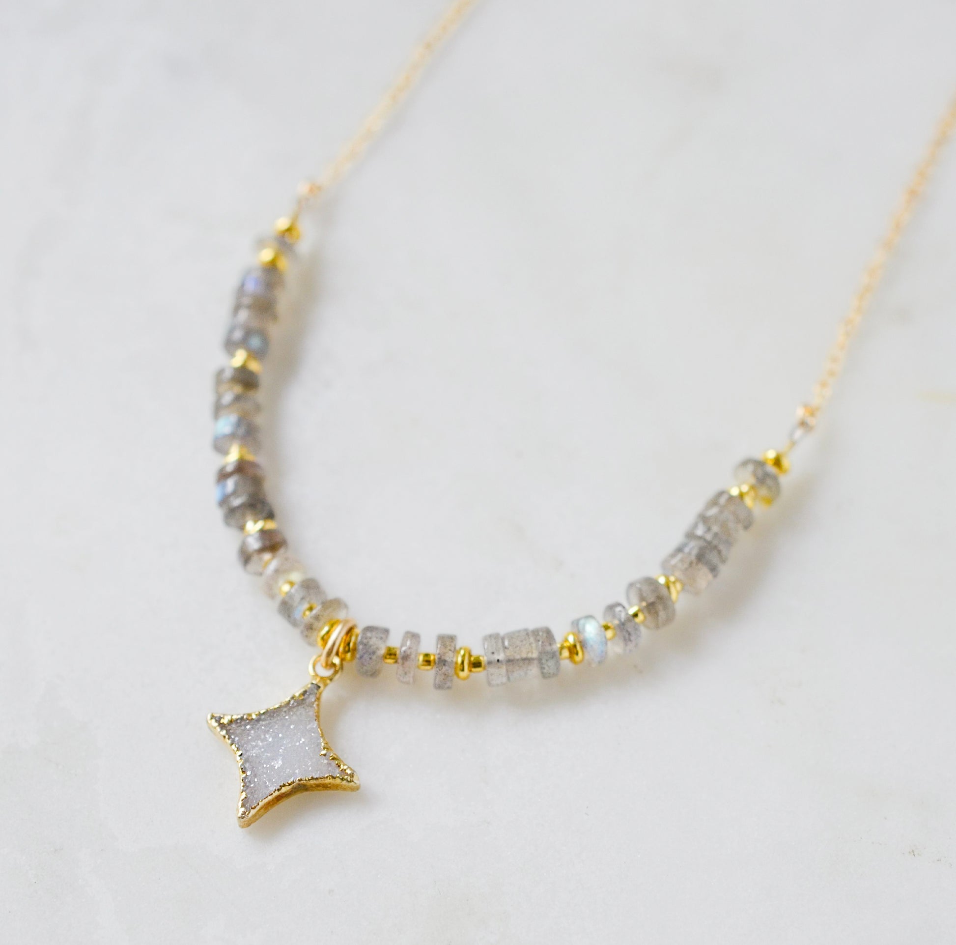 A beaded labradorite gemstone necklace with a white quartz druzy north star pendant at its center. Shown in gold.