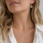 A woman wearing a mystic topaz teardrop necklace and earring set in 14k gold filled. The dainty crystals are clear but shift rainbow colors with movement. Also available in sterling silver.