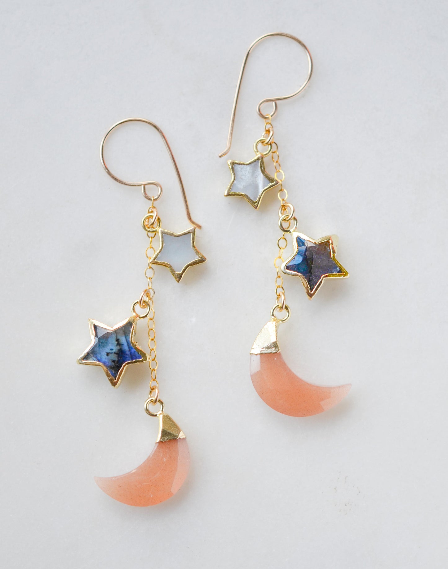 Mother of pearl, Labradorite, and Peach Moonstone moon and star dangle earrings in gold. Each earring has two stars hanging over a peach moonstone crescent.