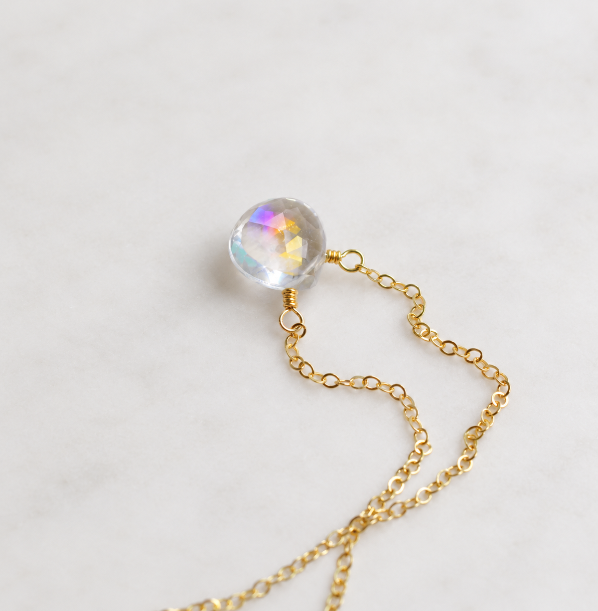 A gold chain necklace featuring a faceted, iridescent, clear mystic topaz teardrop pendant, on a 14k gold filled cable chain. The stone shifts rainbow colors with movement. Also available in sterling silver.