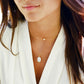 Modeled image of a woman wearing a natural white mother of pearl pendant, layered with a white freshwater pearl chain necklace. Each minimalist necklace is handmade by Gemnia in Connecticut.