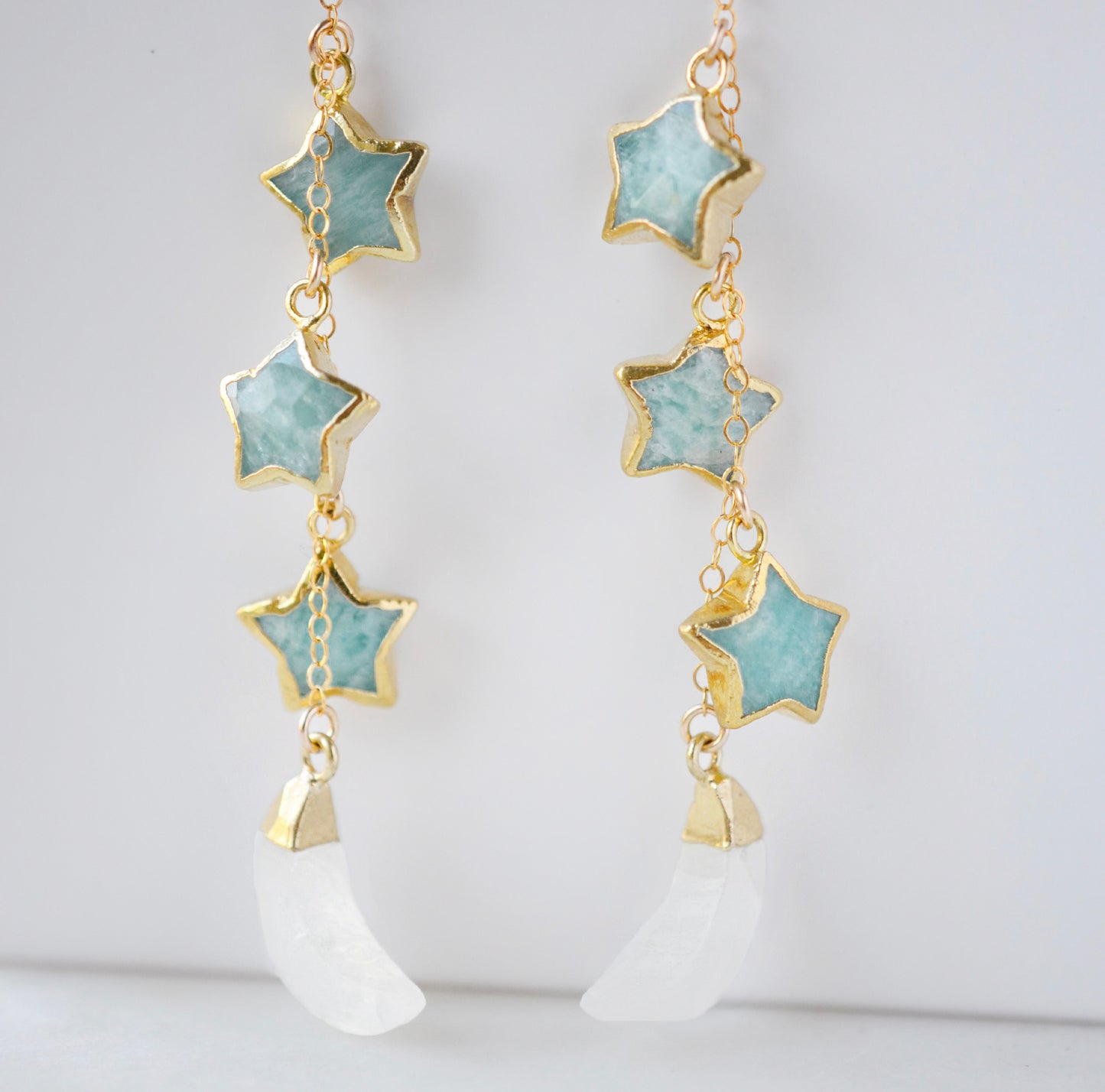 blue amazonite star earrings in gold with rainbow moonstone crescents. Each earring has three gemstone stars and one moon dangling from it.