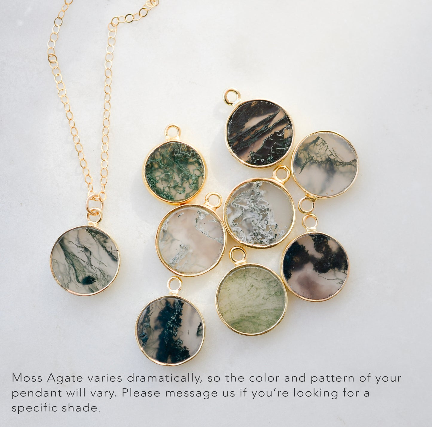 A dainty stone necklace with moss agate pendant on a light background. Shown with other stones to explain color variation. Each stone is different with some having a lot of moss, or dendritic, inclusions, while others are more clear with minimal green inclusions. This necklace is handmade in Connecticut by Gemnia Jewelry.