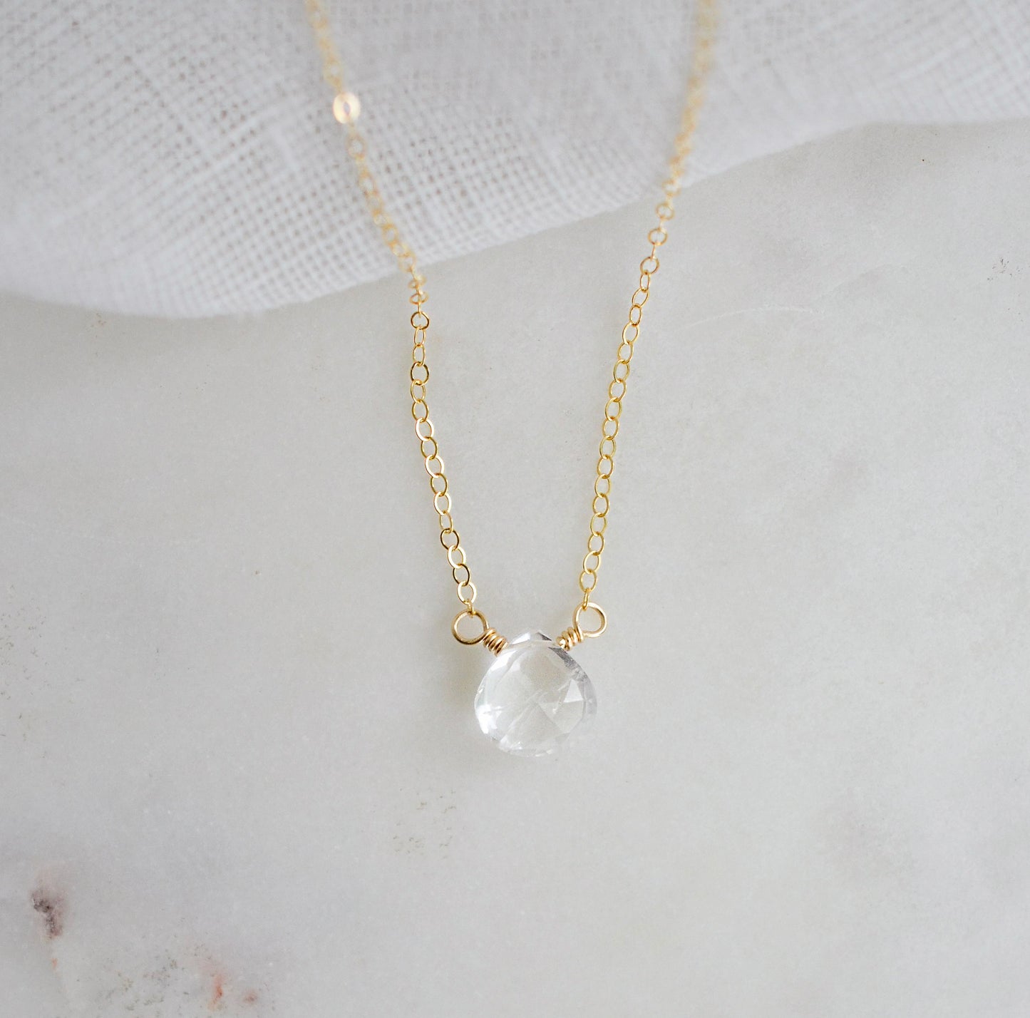 A clear, natural crystal quartz faceted teardrop set onto a 14k gold filled chain.