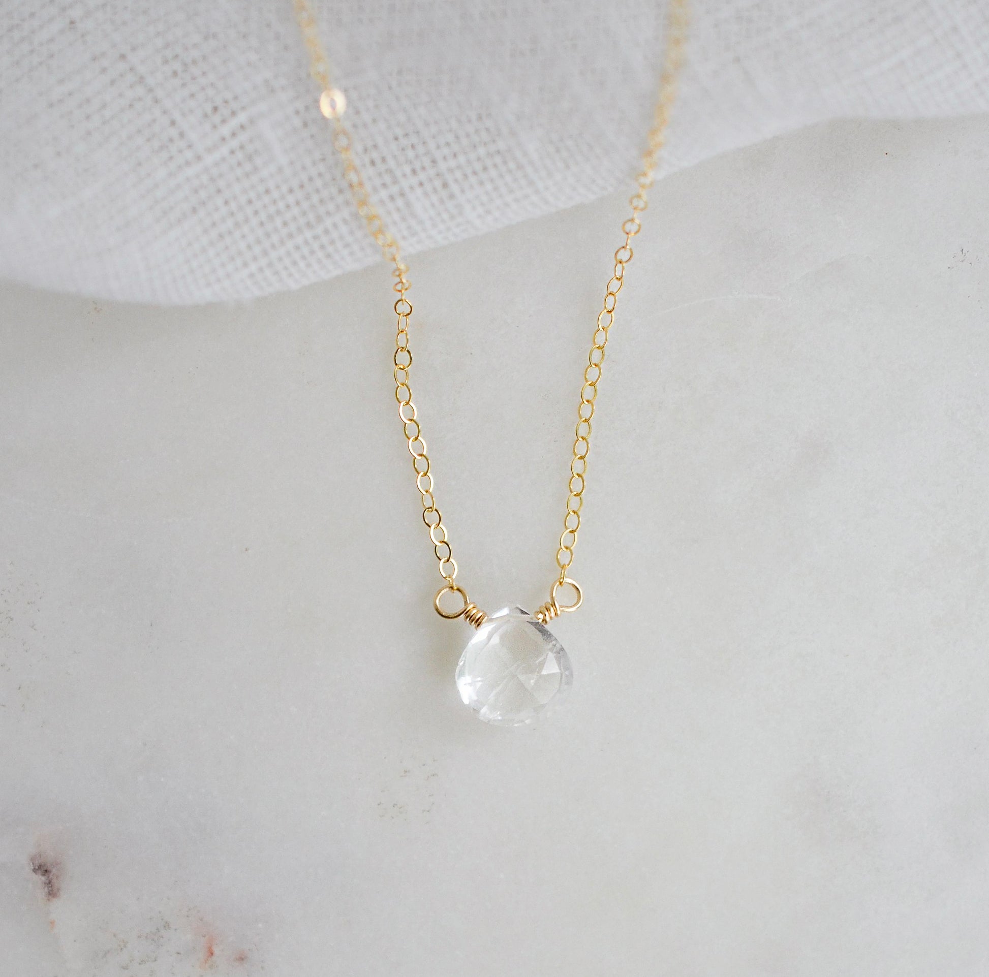 A clear, natural crystal quartz faceted teardrop set onto a 14k gold filled chain.