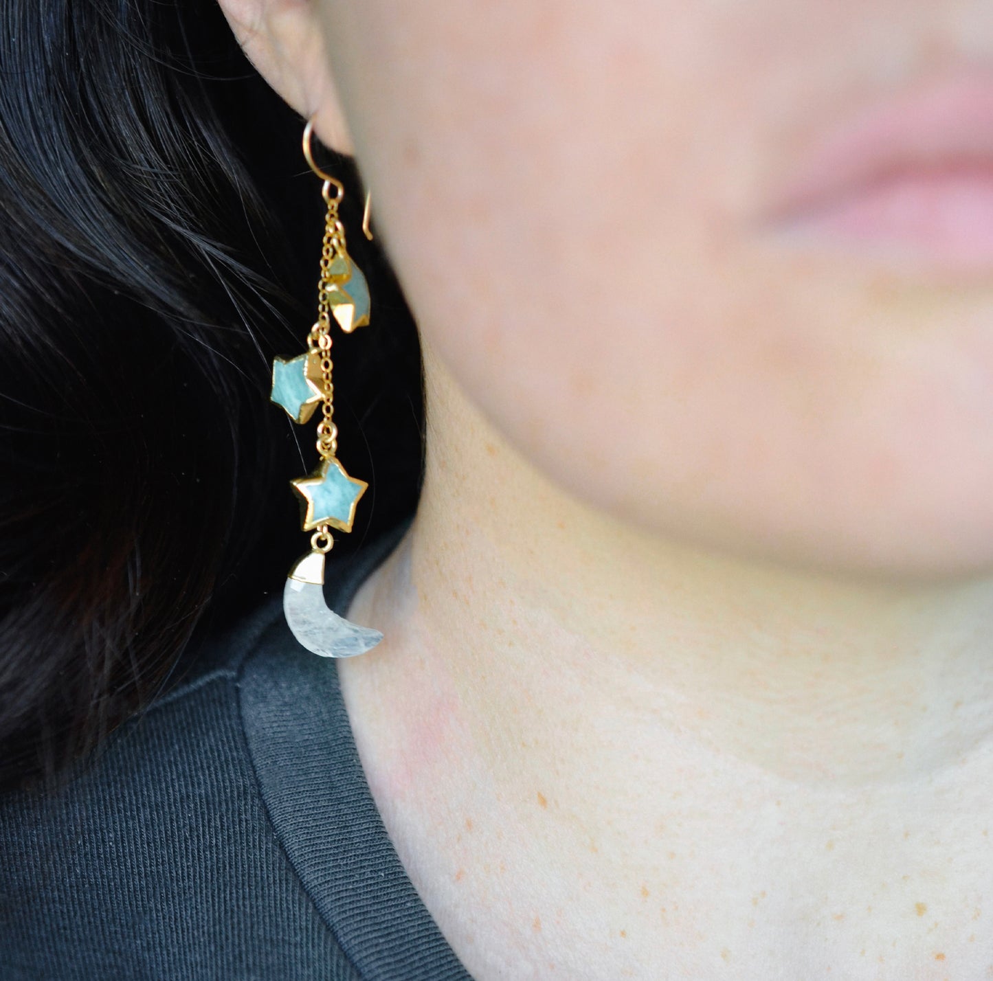 blue amazonite star earrings in gold with rainbow moonstone crescents. Each earring has three gemstone stars and one moon dangling from it. Modeled image.