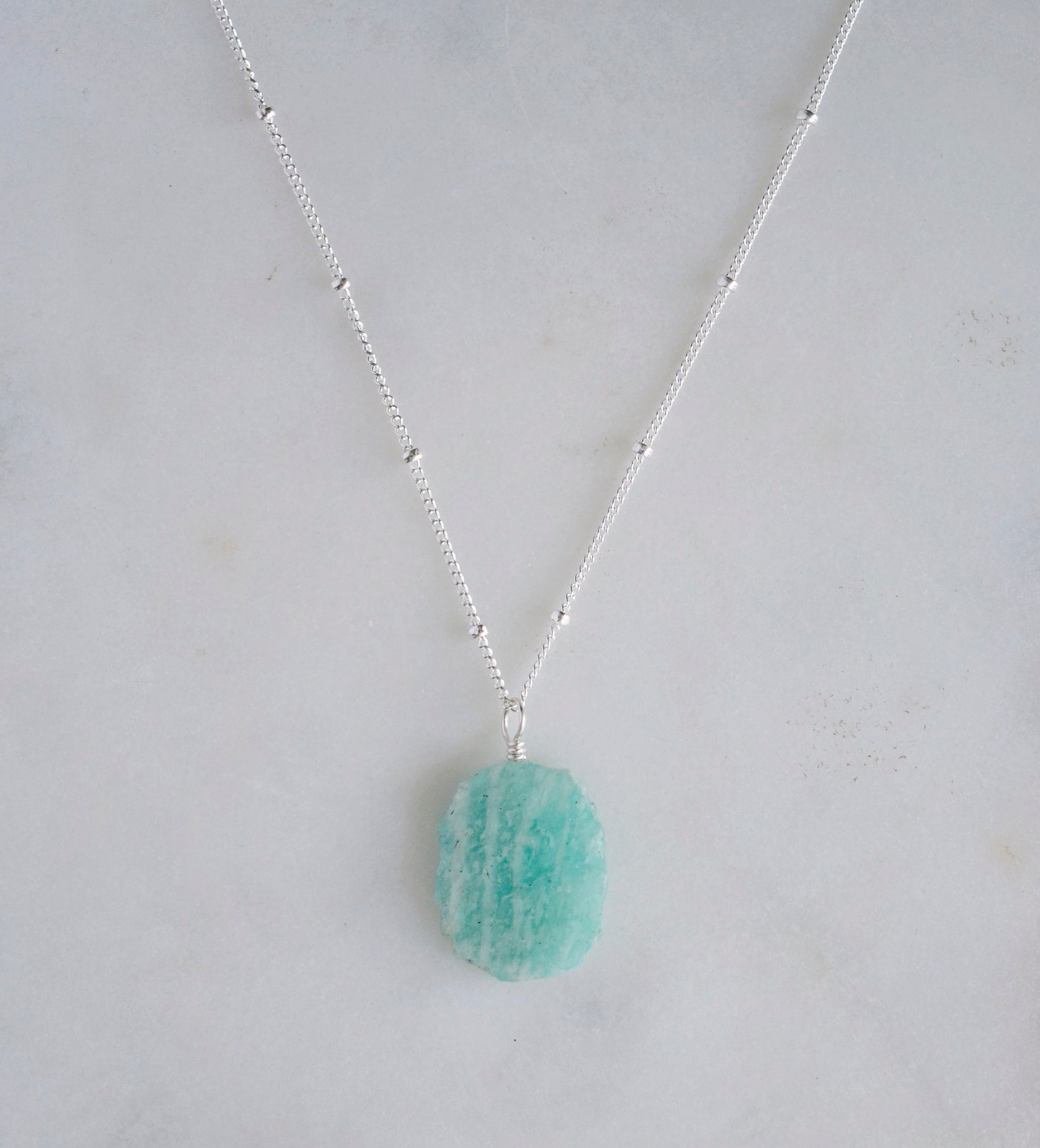 Aqua blue amazonite slice gemstone set onto a sterling silver chain. The stone is semi oval in shape, but irregular. It's smooth polished, but with raw edges. 