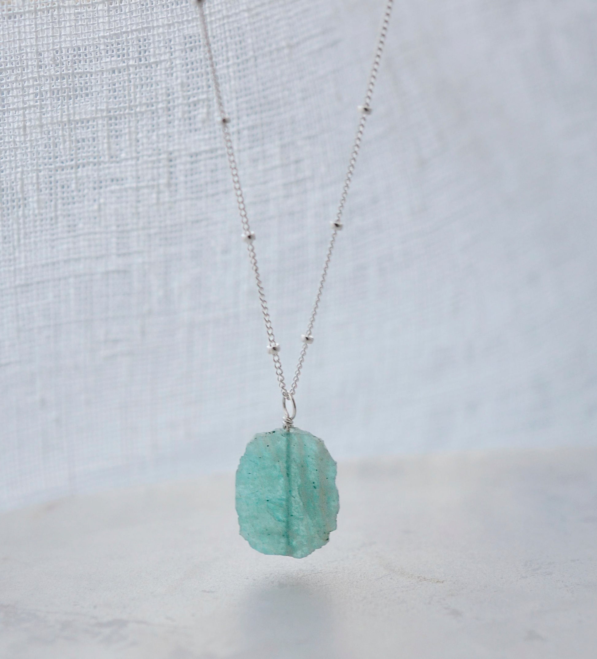 Bright aqua blue Amazonite stone cut into a thin, polished slice with raw edges, then set onto a sterling silver beaded chain.