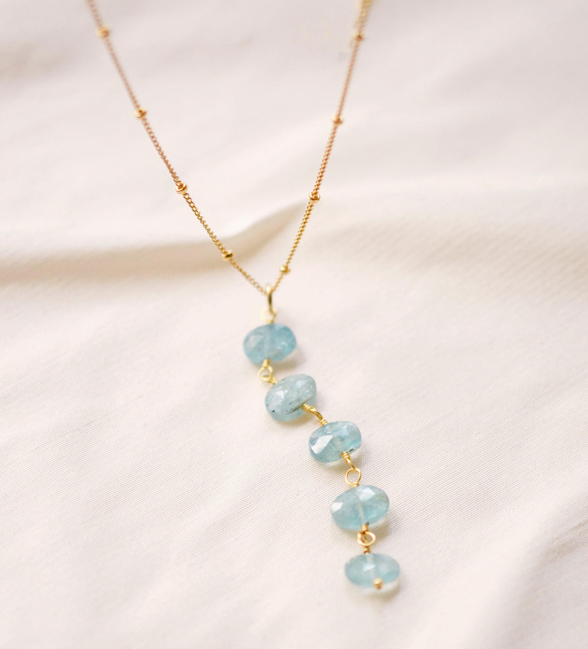Genuine aqua blue Apatite gemstones set onto a beaded gold chain. The stones are flat faceted ovals and vary in aqua hues.