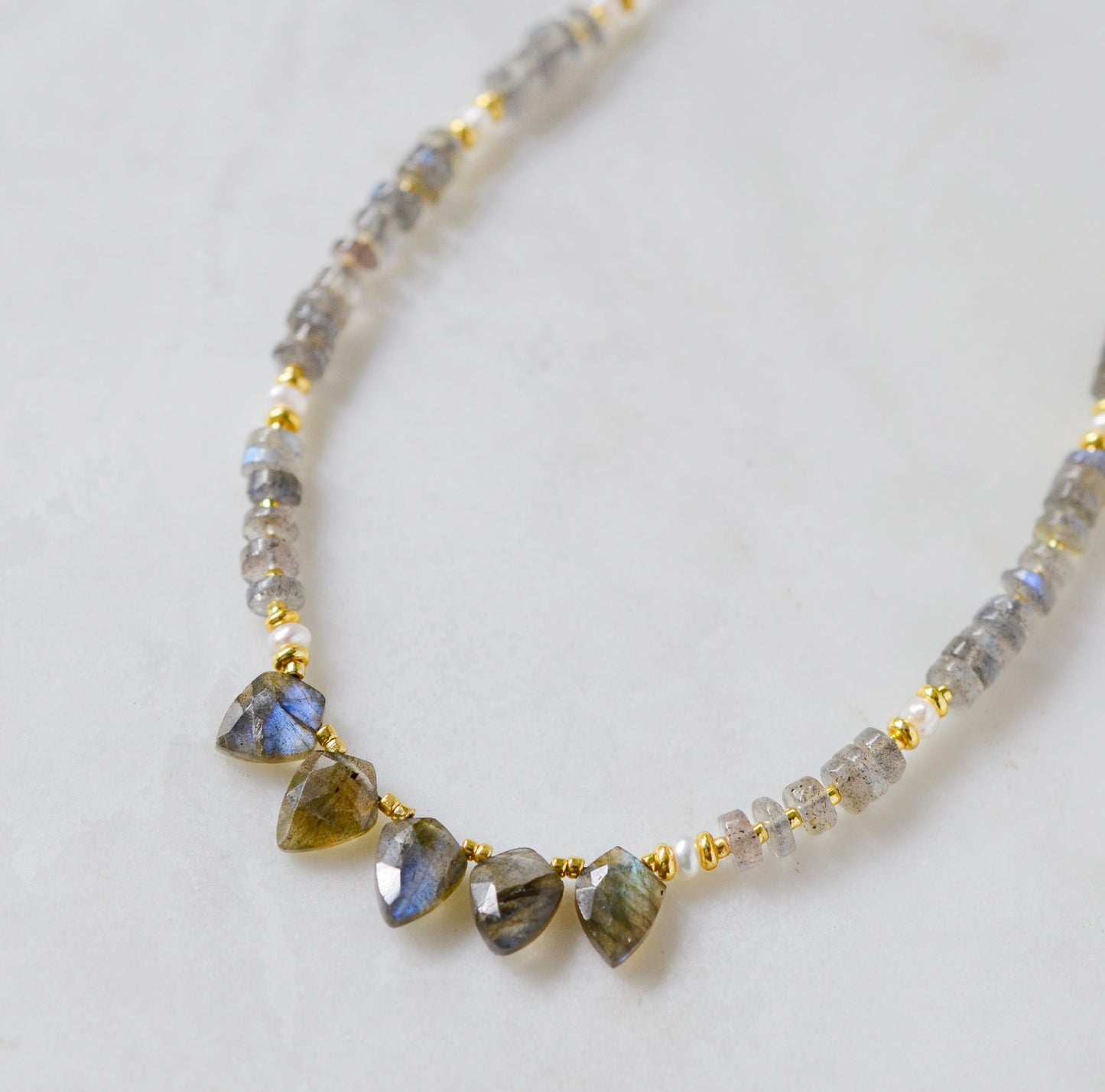A close up of a handmade, beaded labradorite and pearl dainty necklace in gold. 