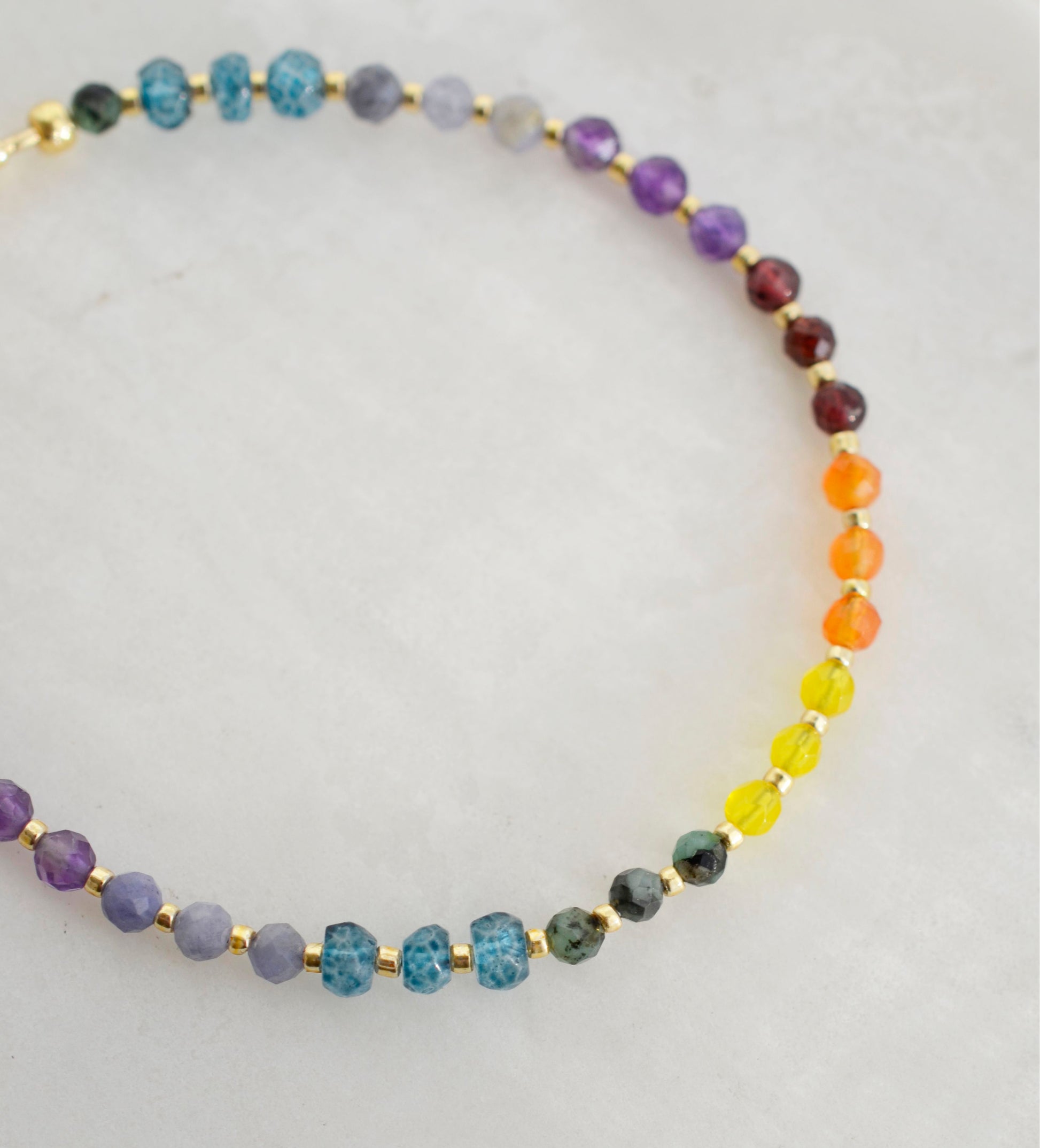 Beaded gemstone bracelet in rainbow colors. Handmade with natural gemstones including: yellow agate, orange carnelian, wine-red garnet, amethyst, tanzanite, topaz, and green emerald. Shown with a gold clasp.