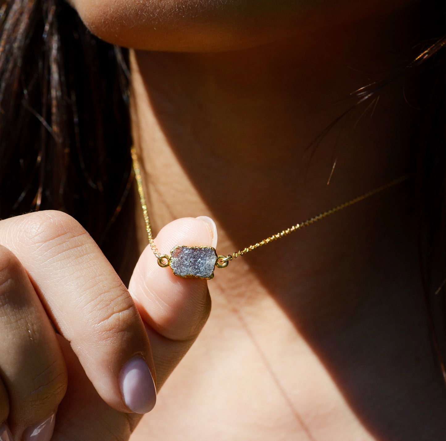 A close up of a natural gray-black quartz druzy gemstone set on a 14k gold filled dainty chain.