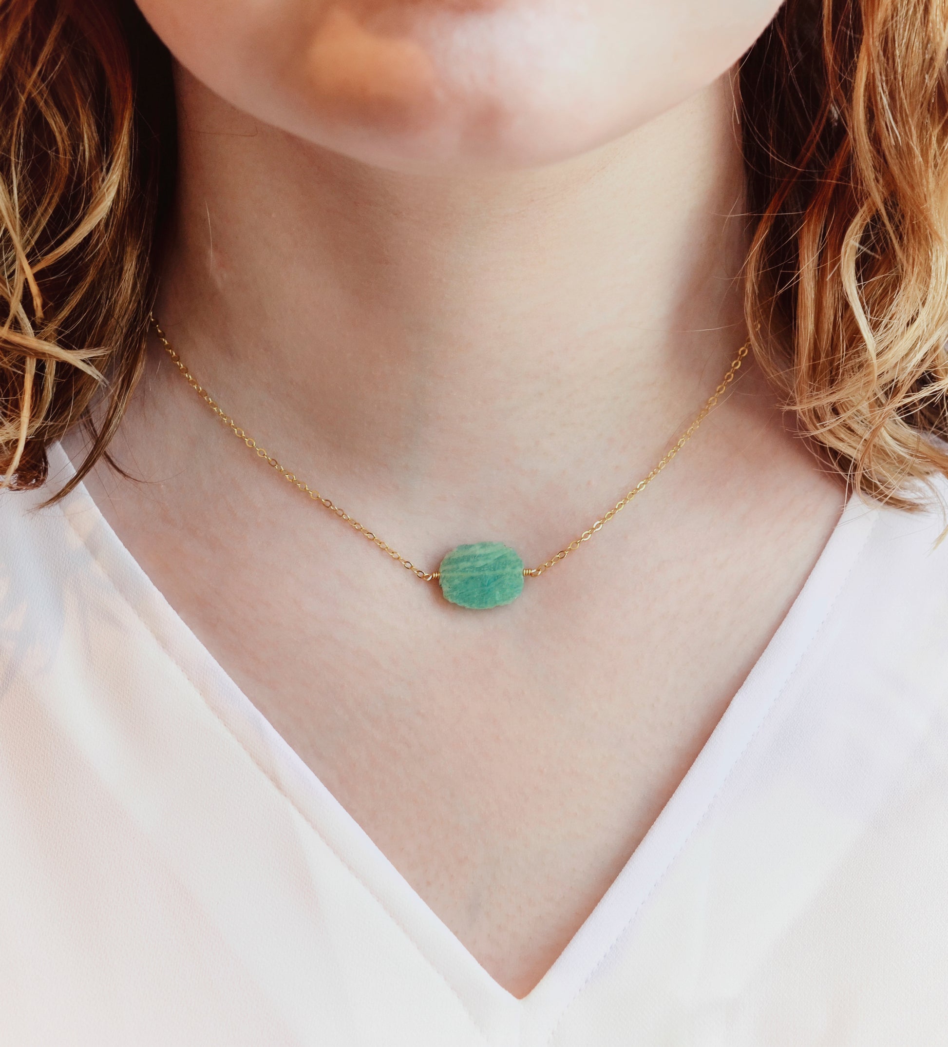 Aqua blue amazonite slice gemstone set onto a 14k gold filled chain. The stone is semi oval in shape, but irregular. It's smooth polished, but with raw edges. Modeled image.