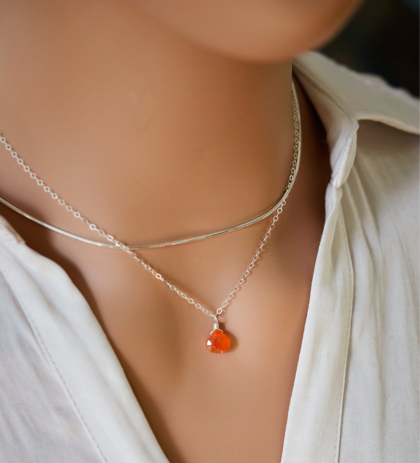 Natural orange Carnelian teardrop gemstone set onto a sterling silver chain. Modeled image.