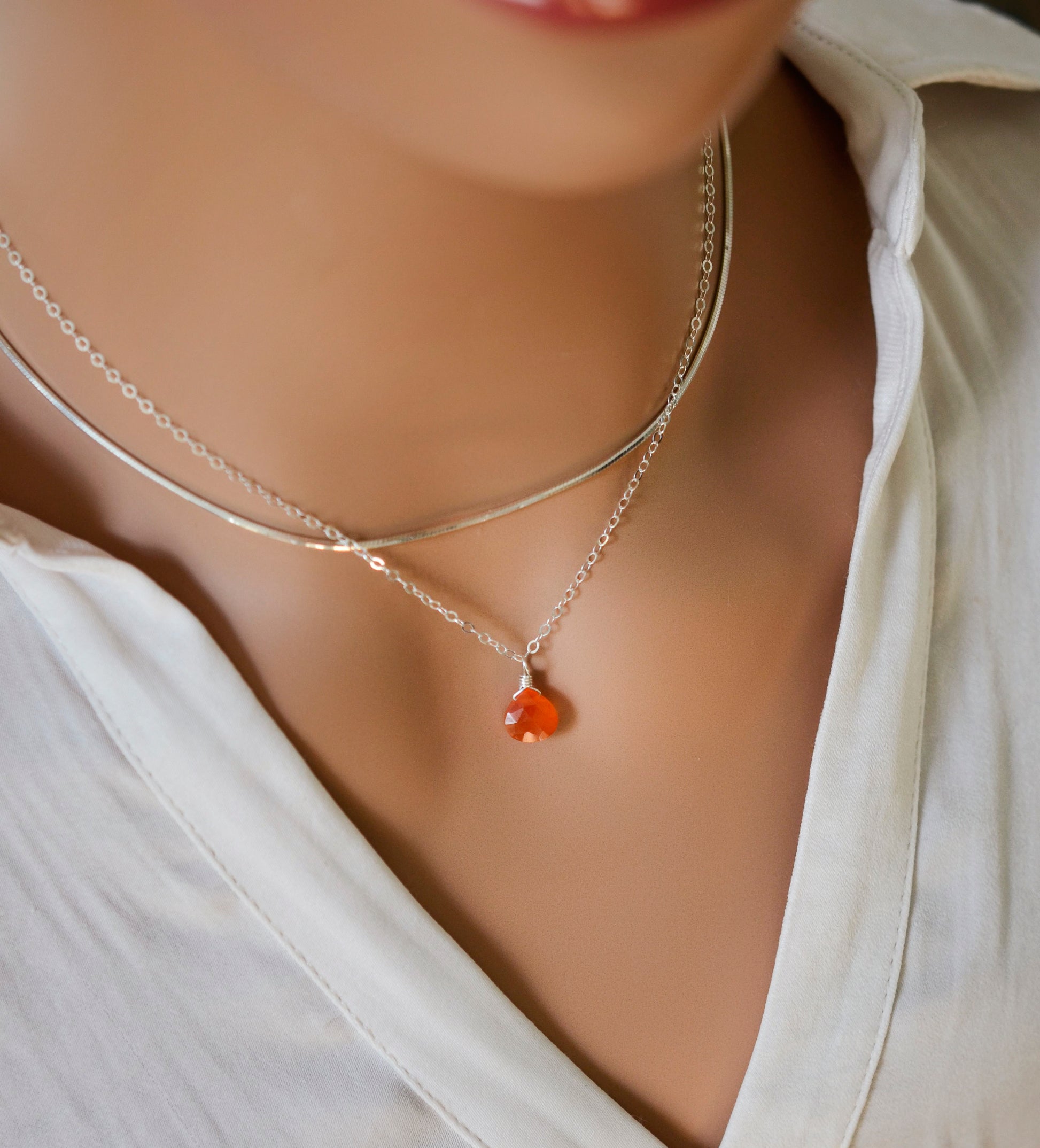 Natural orange Carnelian teardrop gemstone set onto a sterling silver chain. Modeled image.