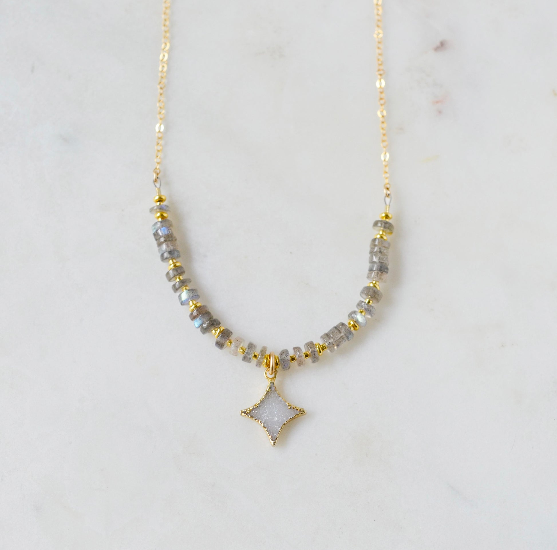 A beaded labradorite gemstone necklace with a white quartz druzy north star pendant at its center. Shown in gold.
