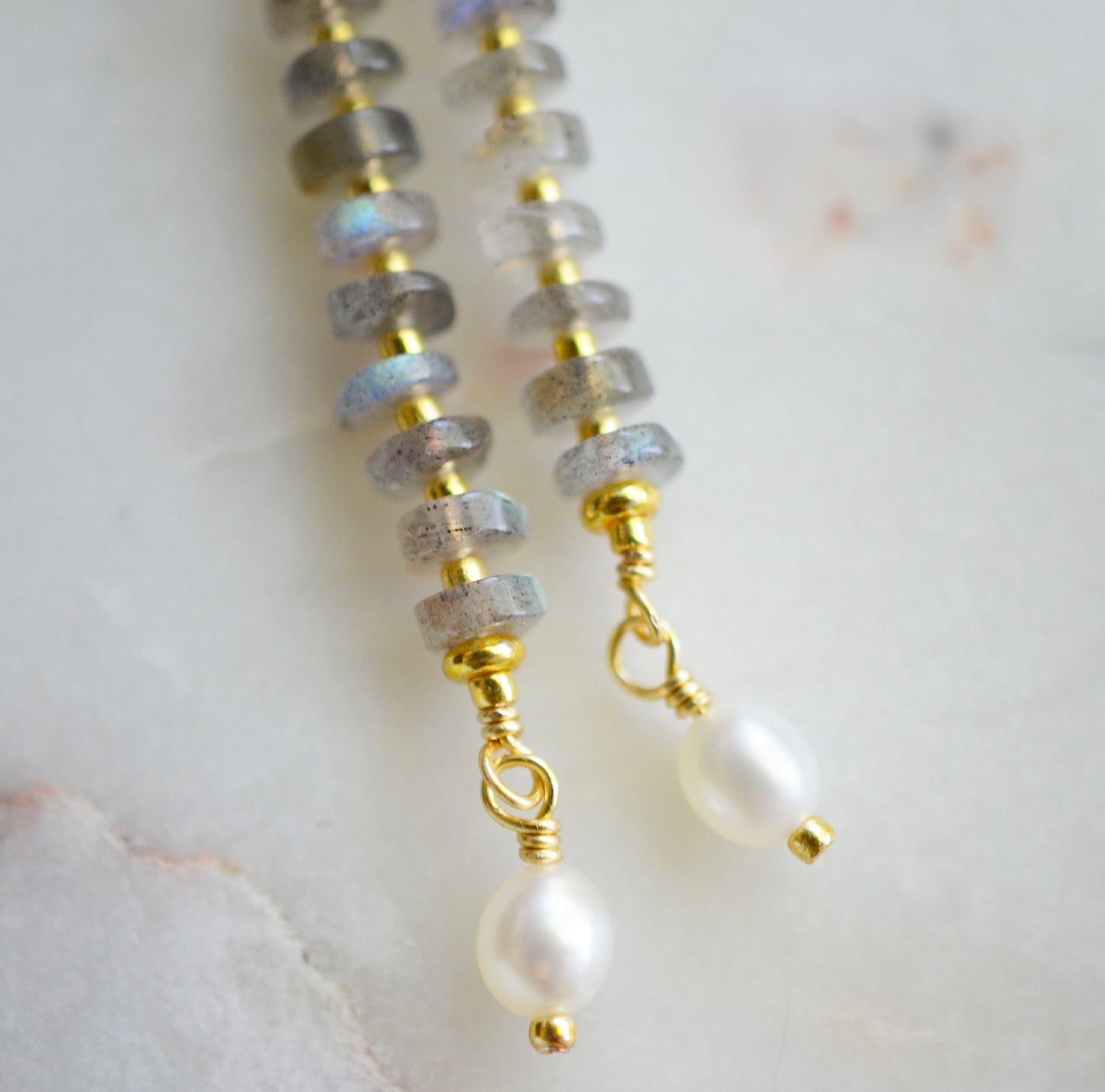 Handmade beaded dangle earrings with labradorite and white freshwater pearls. The earrings are a long bar style with dainty pearls on the bottom. The gemstones flash blue and green.