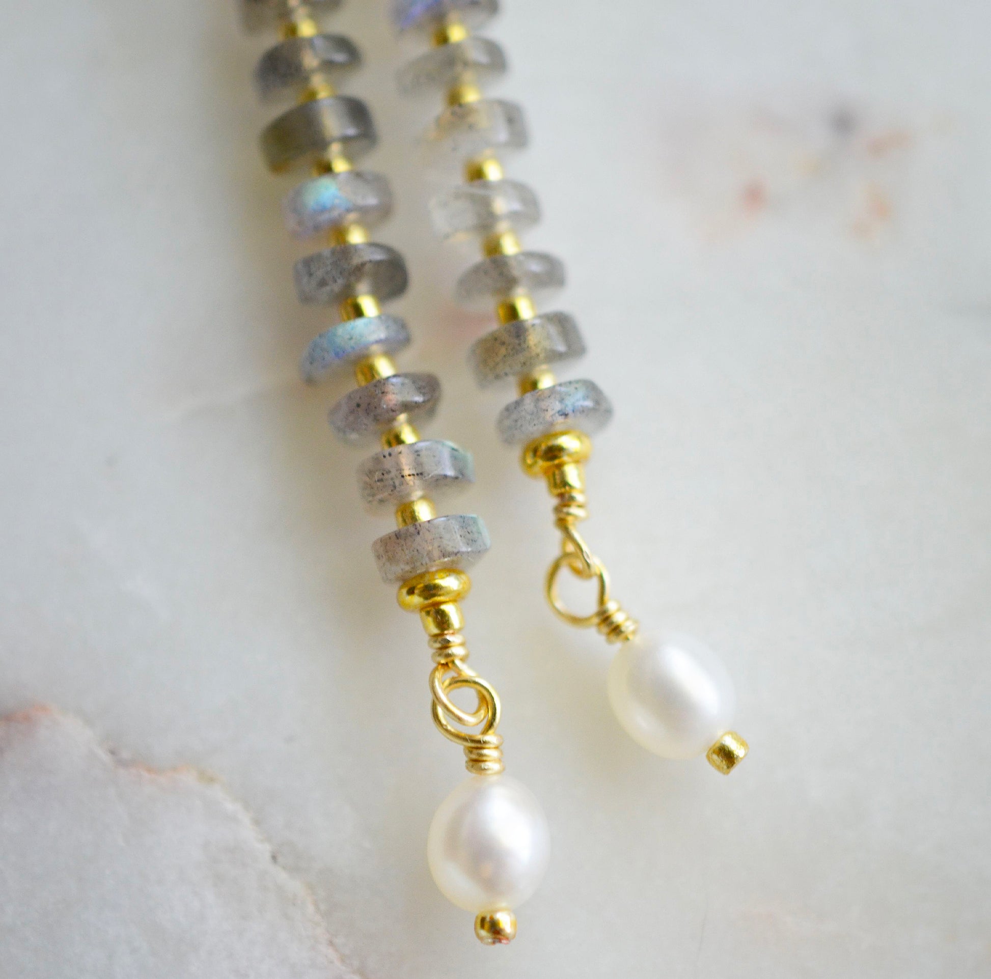 Handmade beaded dangle earrings with labradorite and white freshwater pearls. The earrings are a long bar style with dainty pearls on the bottom. The gemstones flash blue and green.