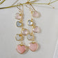 Long pink stone heart earrings in 14k gold filled. There are five heart crystal dangles hanging from a simple chain forming a cluster. The stones include: rose quartz, mother of pearl, pink opal, and rainbow moonstone. They are approximately three inches long.