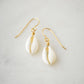 A natural off-white cowrie shell hangs from an earring hook. Shown in gold.