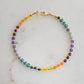 Beaded gemstone bracelet in rainbow colors. Handmade with natural gemstones including: yellow agate, orange carnelian, wine-red garnet, amethyst, tanzanite, topaz, and green emerald. Shown with a gold clasp.