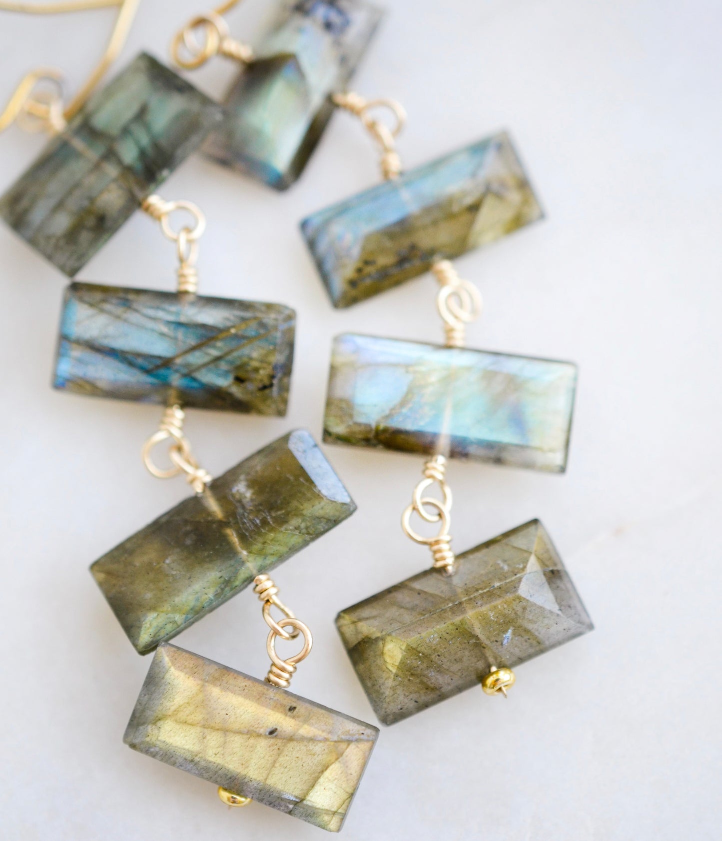 Close up image: Four faceted emerald cut labradorite gemstones dangle in these 14k gold filled earrings. Each stone flashes blue or green.