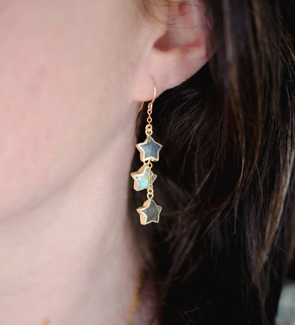 A woman wearing long labradorite earrings with three gemstone stars set in gold. These celestial dangles are handmade in gold or sterling silver by Gemnia in New England.