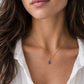 A woman wearing a minimalist genuine tanzanite gemstone droplet on a 14k gold filled chain. The natural gem is smooth polished and periwinkle in color. Handmade in Connecticut by Gemnia.