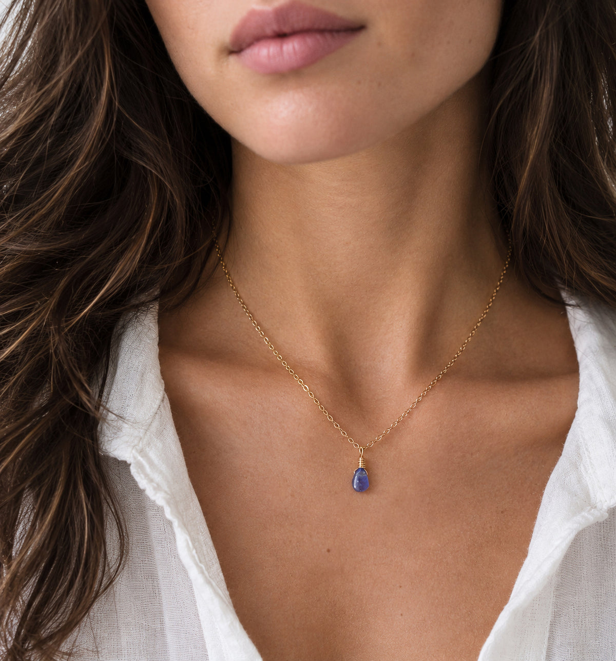 A woman wearing a minimalist genuine tanzanite gemstone droplet on a 14k gold filled chain. The natural gem is smooth polished and periwinkle in color. Handmade in Connecticut by Gemnia.