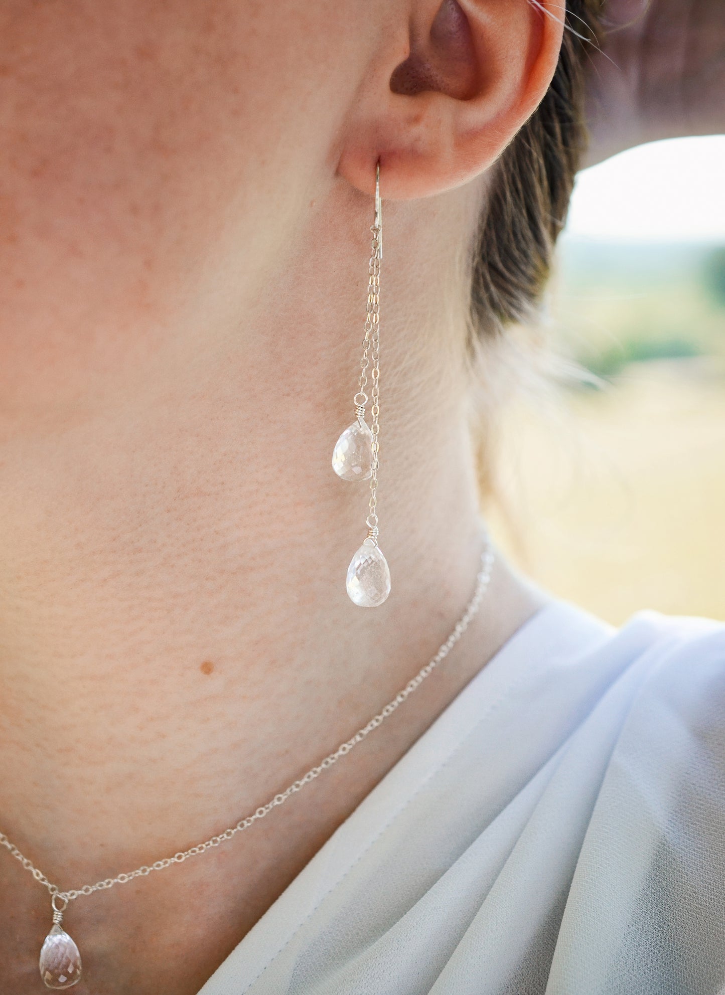 Long clear crystal quartz earrings with two teardrop dangles hanging from a dainty chain. Modeled in sterling silver with the matching necklace.