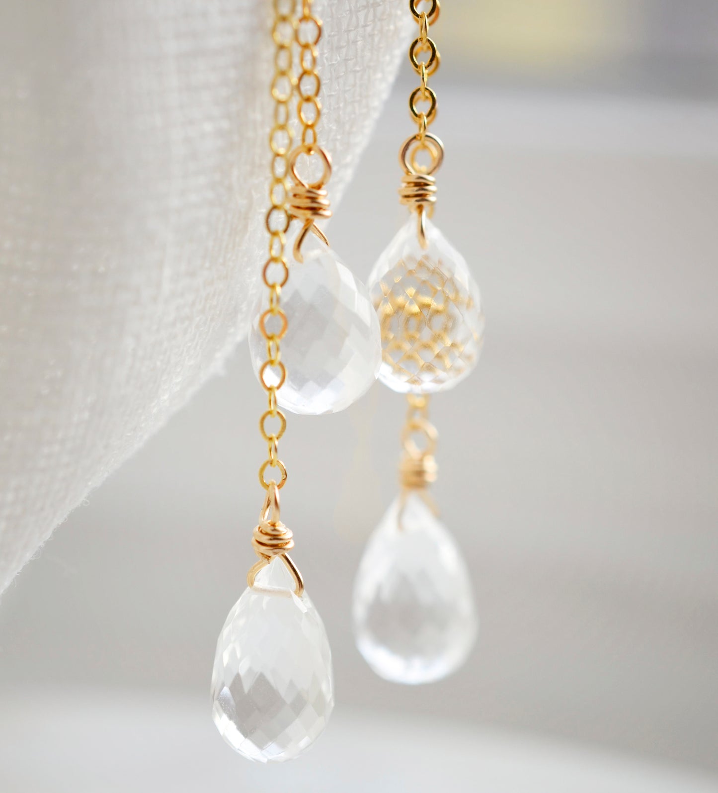 Long clear crystal quartz earrings with two teardrop dangles hanging from a dainty 14k gold filled chain. Close up of gemstones.