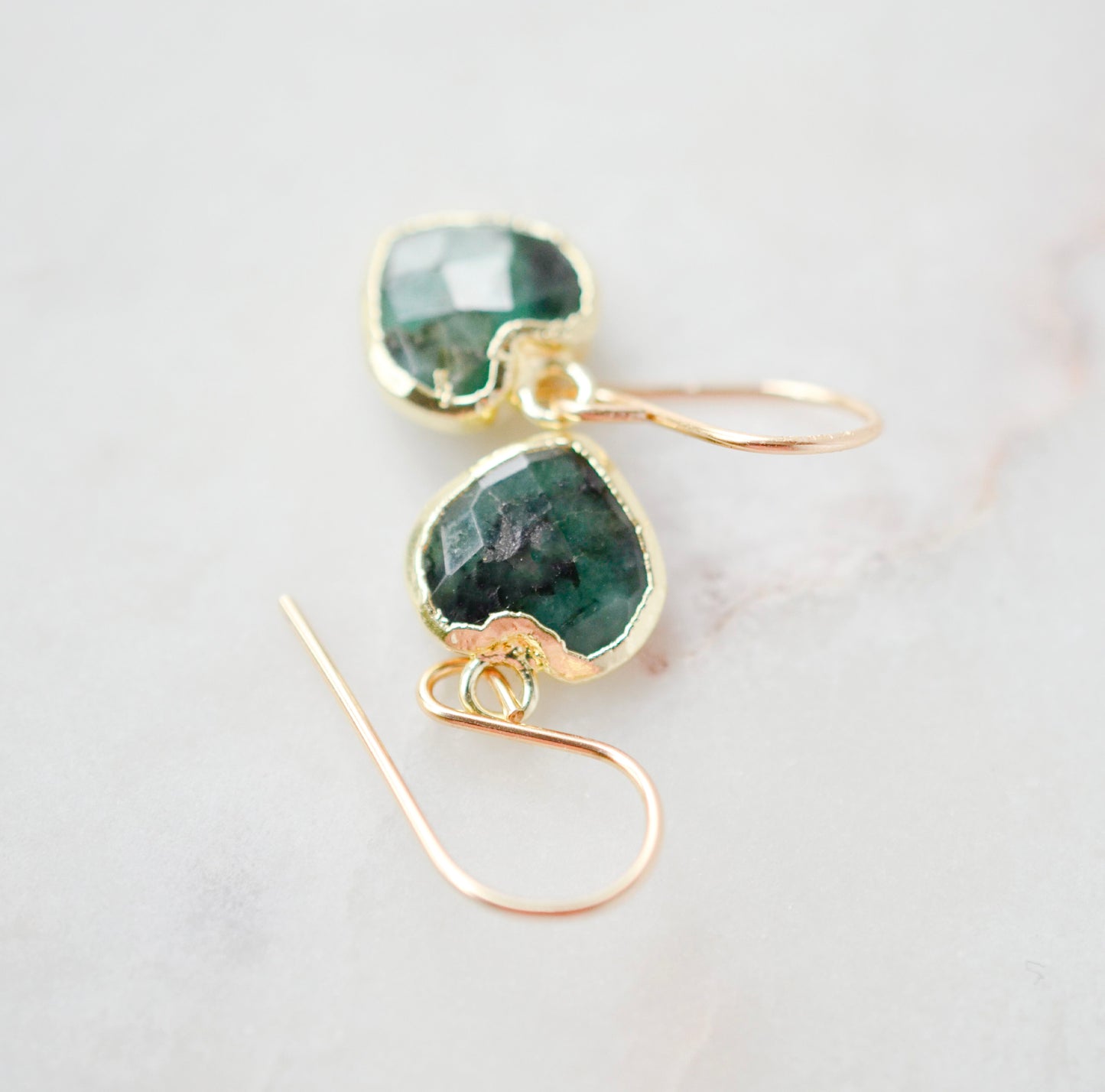 Raw emerald heart earrings in gold. The stones are bezeled in 22k gold then set on gold earwires. The gemstone colors range in dark greens with hints of white or black. Top View.