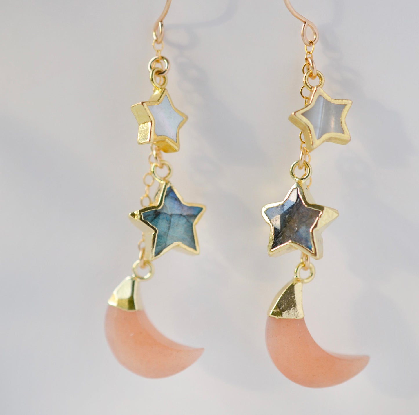 Mother of pearl, Labradorite, and Peach Moonstone moon and star dangle earrings in gold. Each earring has two stars hanging over a peach moonstone crescent.