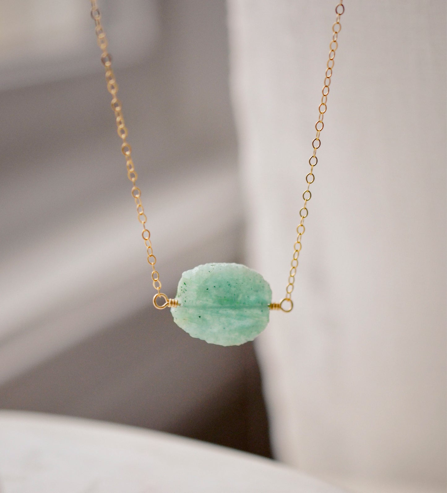 Aqua blue amazonite slice gemstone set onto a 14k gold filled chain. The stone is semi oval in shape, but irregular. It's smooth polished, but with raw edges.