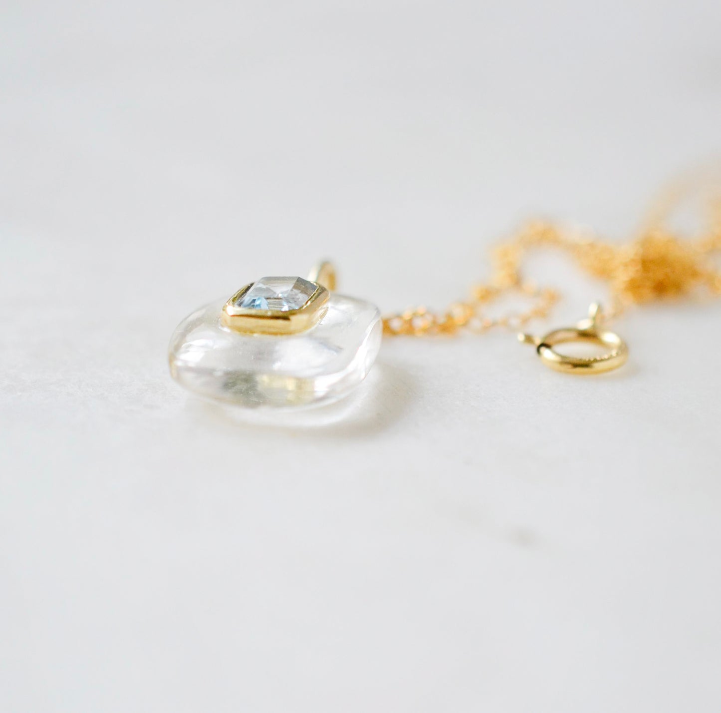 Side view. Handmade Maris necklace featuring a Blue Topaz set inside a clear Rock Crystal frame on a 14K Gold Filled chain. Ideal gift for wife, girlfriend, or mom. Minimalist topaz pendant for layering.