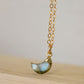 A close up image of a natural labradorite gemstone shaped in a crescent moon and set on a 14k gold filled chain. 