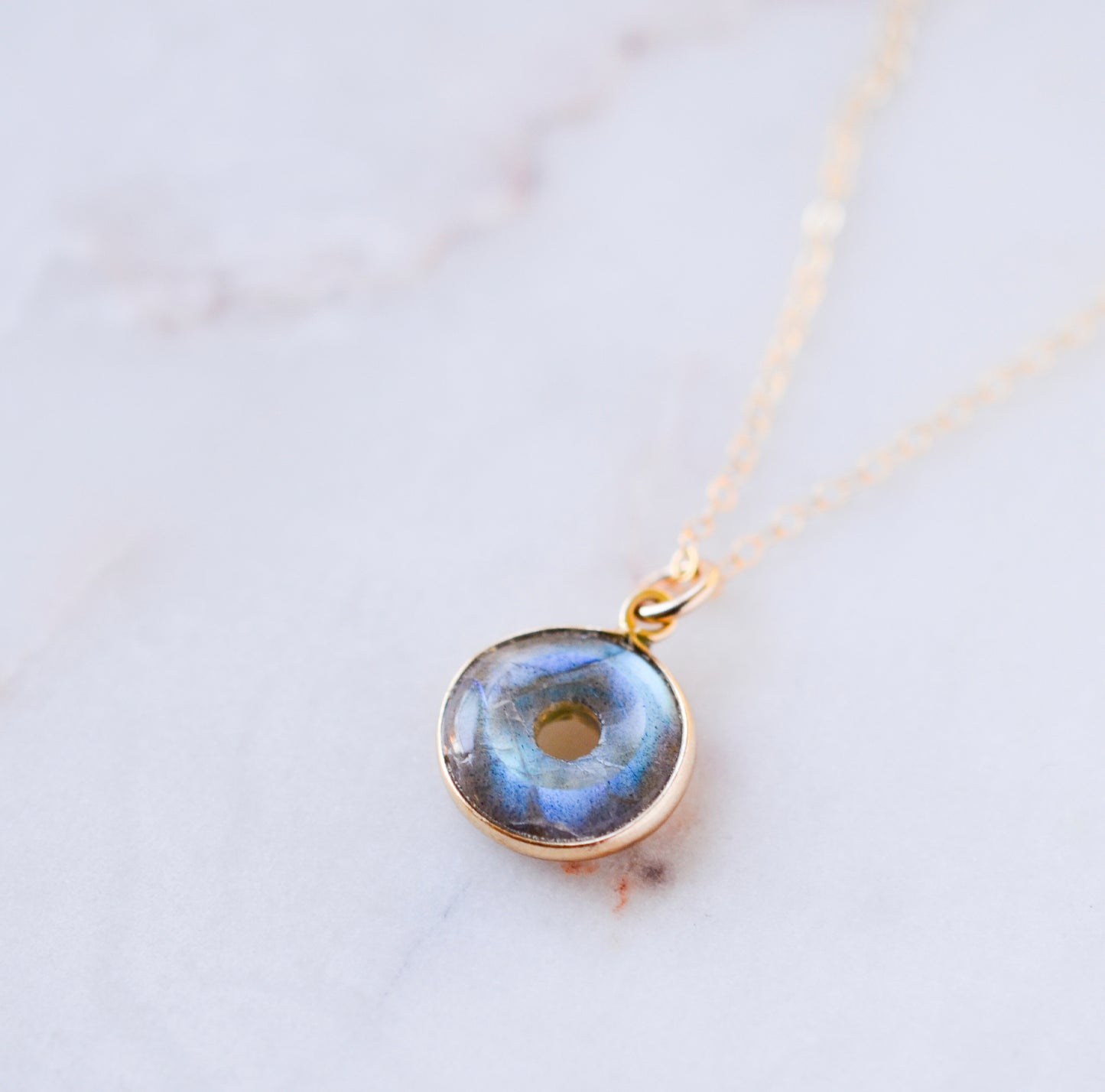 A handmade blue and green flash labradorite stone pendant in a smooth polished doughnut shape set on a 14k gold filled chain. Handcrafted artisan jewelry from Connecticut by Gemnia.