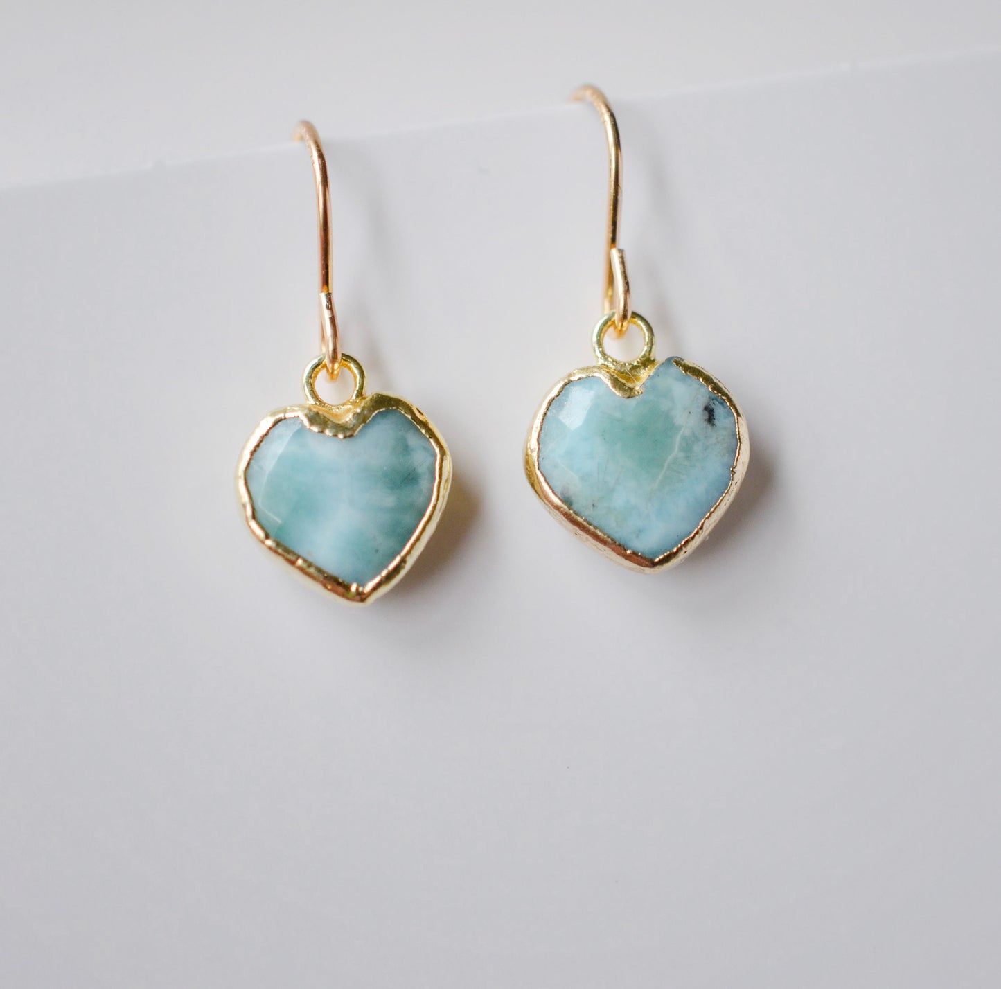 Aqua blue, natural Larimar stone heart earrings in gold. The stones range in blue, white, or green with the occasion mark of brown or black.