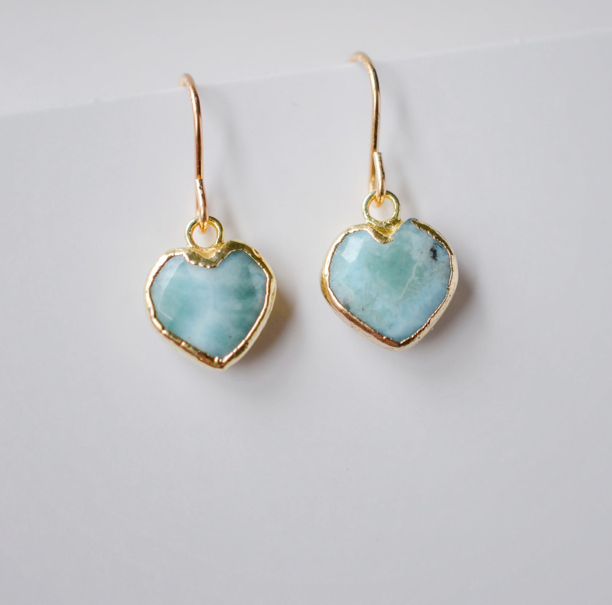 Aqua blue, natural Larimar stone heart earrings in gold. The stones range in blue, white, or green with the occasion mark of brown or black.