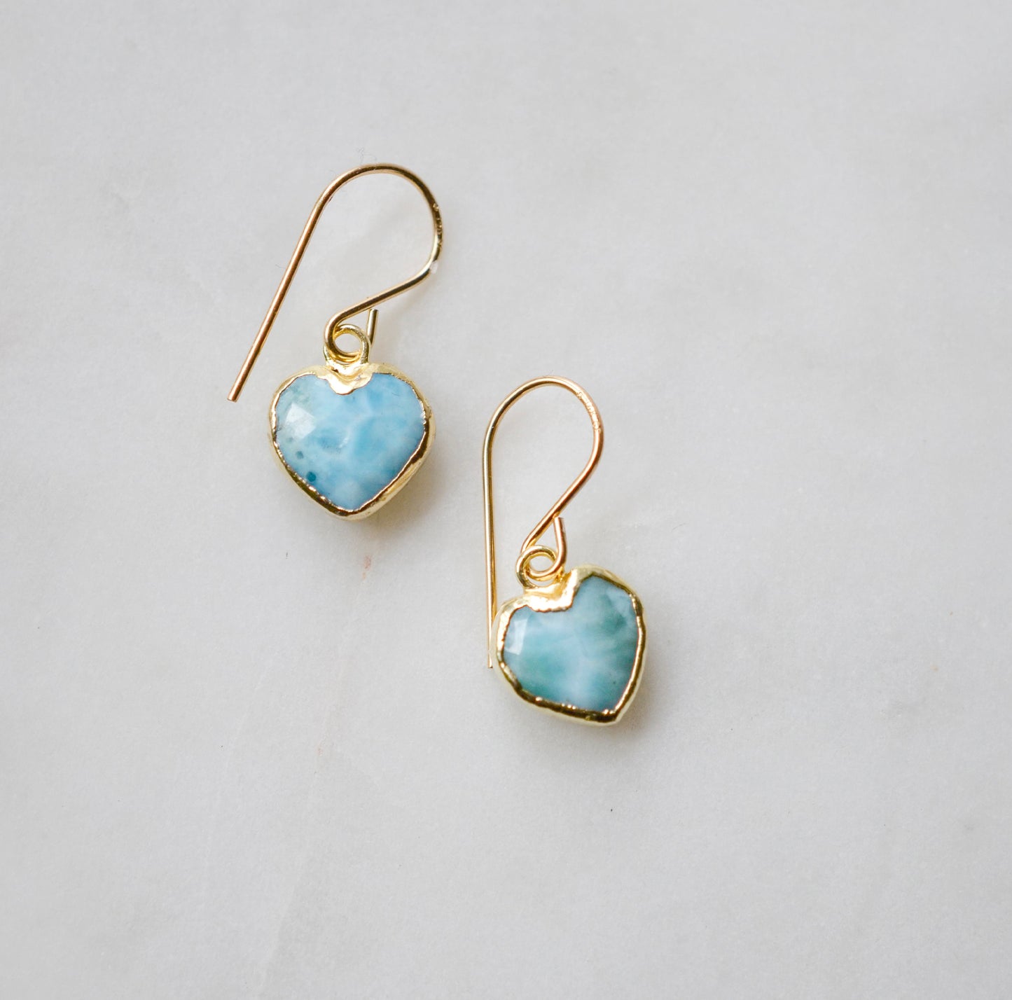 Aqua blue, natural Larimar stone heart earrings in gold. The stones range in blue, white, or green with the occasion mark of brown or black.