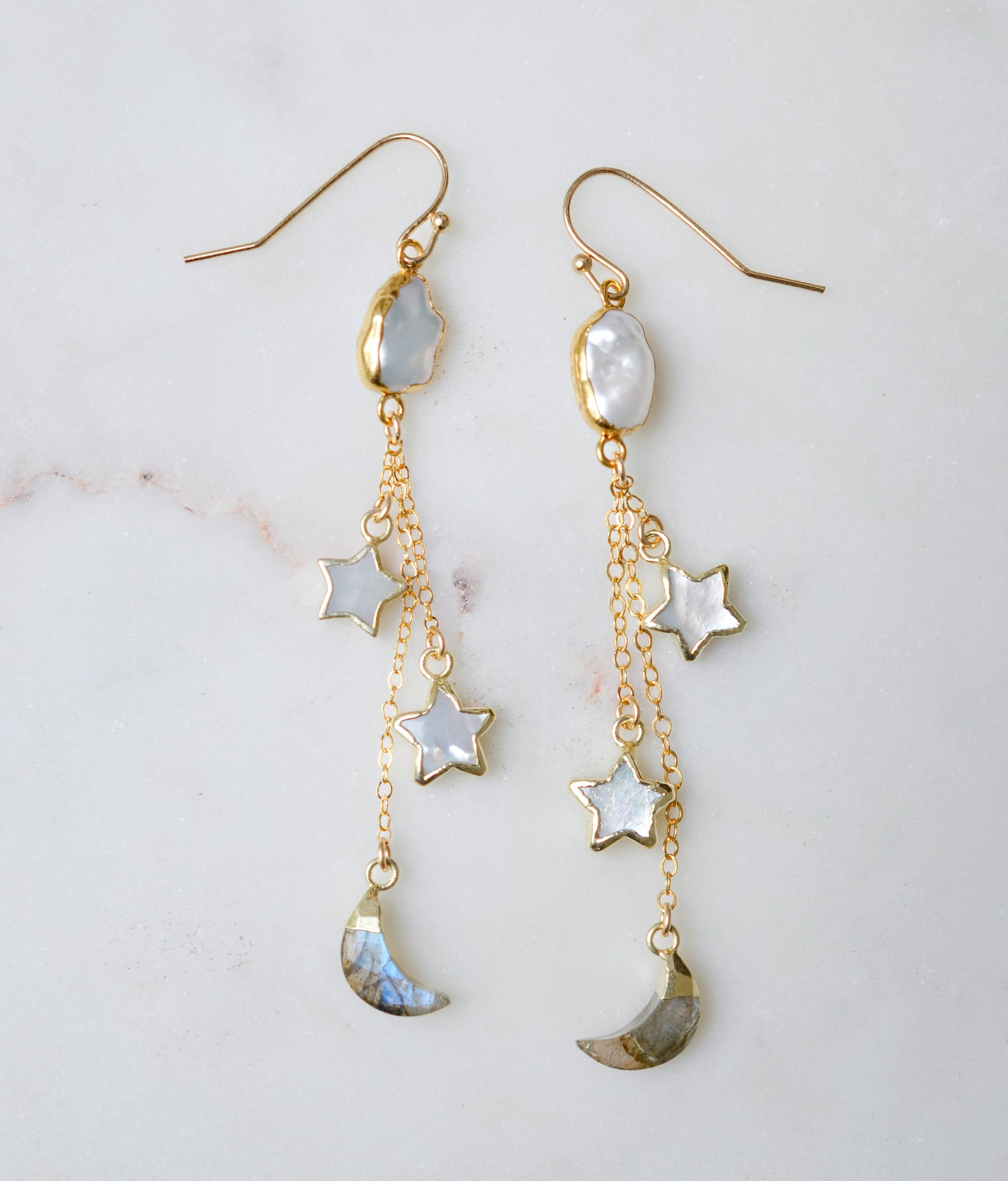 Long gold dangle earrings with star and moon charms on a light background. The stones are freshwater pearl, labradorite, and mother of pearl.
