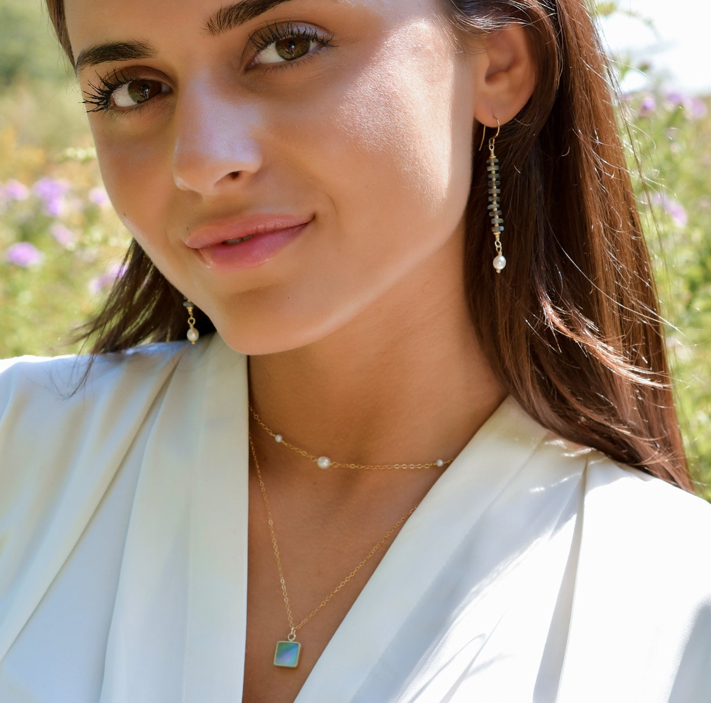 Woman wearing labradorite and pearl earrings alongside layered gemstone necklaces. All jewelry is handmade in Connecticut by Gemnia.