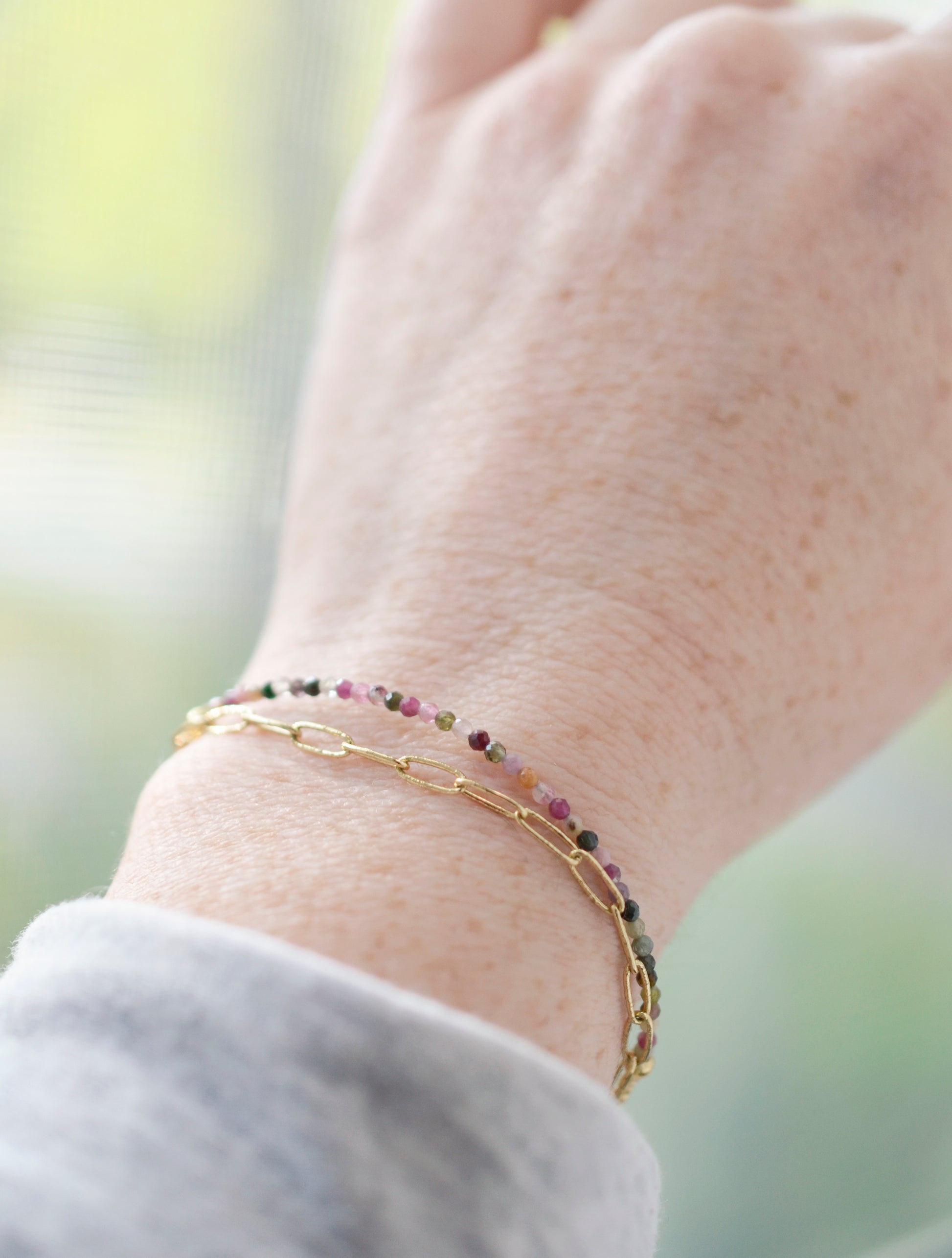Tiny mulit-color Tourmaline faceted round gemstones on a gold beaded bracelet. Modeled image.